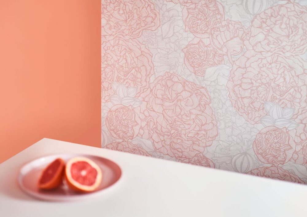The Amalfi-Lines Alcea wallpaper features intricate floral line drawings in soft coral hues, paired with fresh grapefruit on a minimalist table for a harmonious interior look.
