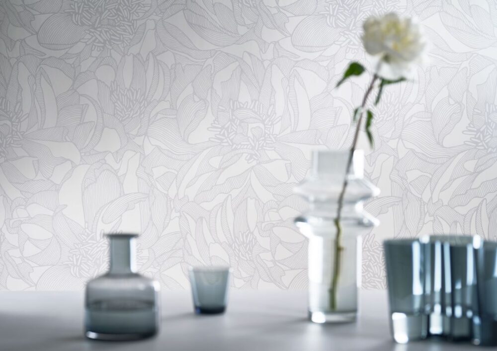The Amalfi-Lines Belissima wallpaper features an elegant floral pattern in soft grey tones, paired with clear glass vases and a single white flower for a minimalist touch.