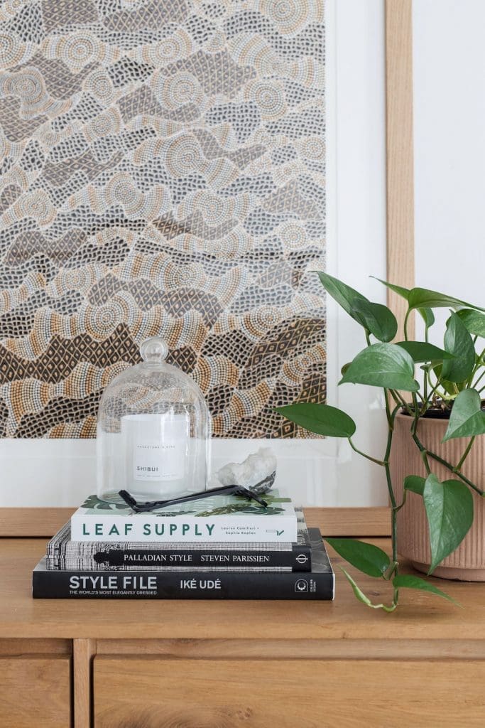 Cement pot, stack of books, candle and glass cloche on sideboard