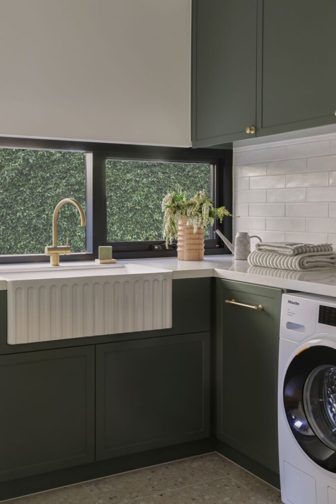 Laundry with green cabinetry farmhouse sink and brass tap