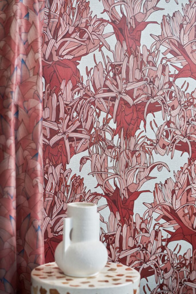 Looking Up - Terra Firma wallpaper featuring bold red and pink floral motifs, complemented by a geometric-patterned table and a white ceramic vase.