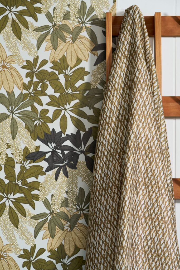 Parasol Leaves - In Sun wallpaper with green and beige botanical designs, paired with a geometric-patterned fabric draped over a wooden ladder.