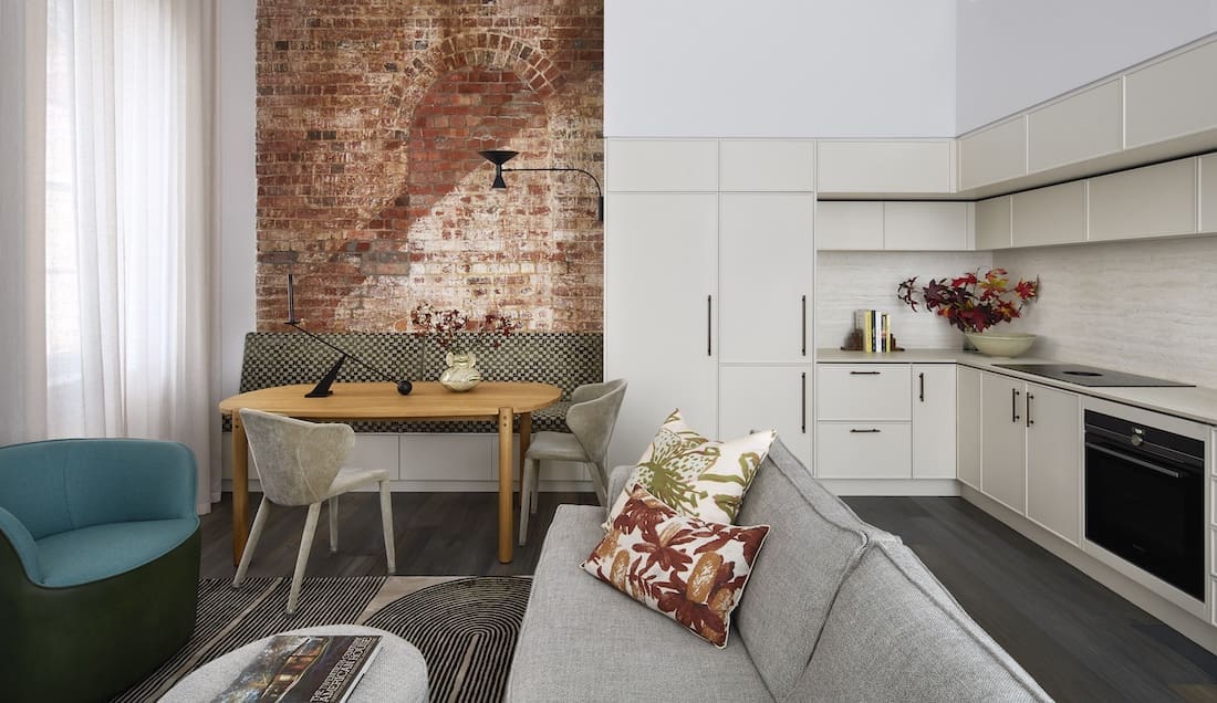 Exposed brick dining nook opening into living and kitchen in Tribeca Brewery apartment by The Stylesmiths